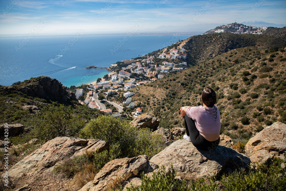 Beautiful woman sitting on a cliff with the mediterranean sea and small coast town in the background