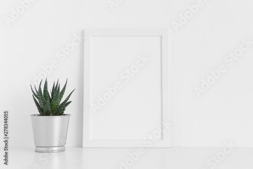 White frame mockup with a cactus in a pot on a white table. Portrait orientation.