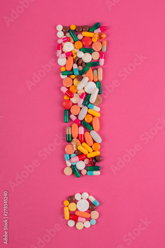 Exclamation mark arranged from assorted pharmaceutical medicine pills, tablets and capsules on pink background