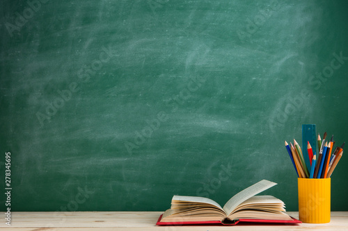 Education and reading concept - group of colorful books on the wooden table in the classroom, blackboard background