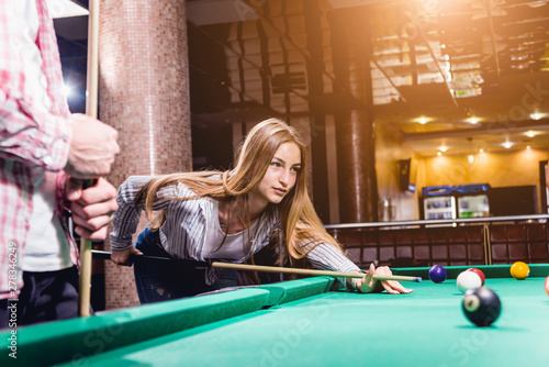 Young woman playing in billiard. Posing near the table with a cue in her hands