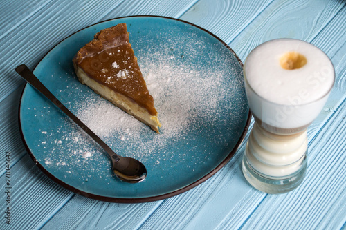 The cheesecake in a plate and latte on a blue wooden table.