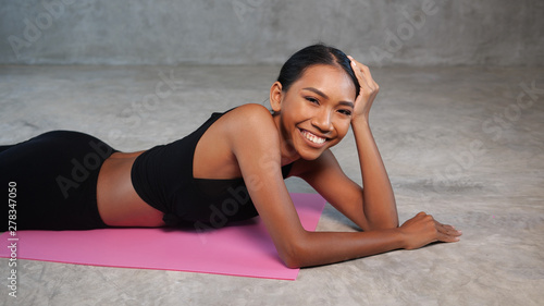 Happy healthy smiling woman relaxing on the pink yoga mat at the gym. Female in sportswear posing at fitness studio