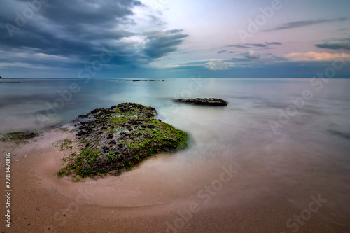 Seascape view of a calm sea with rocks with algae. Beauty sky with clouds at the horizon.