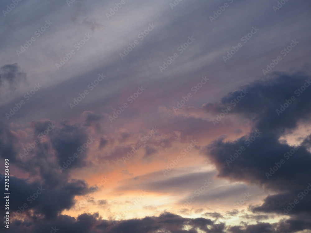 View of the dramatic sky at sunset with dark blue clouds and pink, purple and yellow flashes from the sun's rays