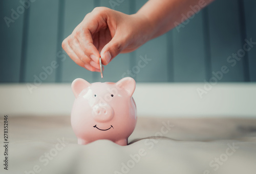 Woman Hand is Putting a Money Coin into Piggy Bank for Savings on The Bedroom., Female Hand is Inserting Coin in Pink Piggybank., Saving for The Finance Future, Business Banking and Financial Concept.