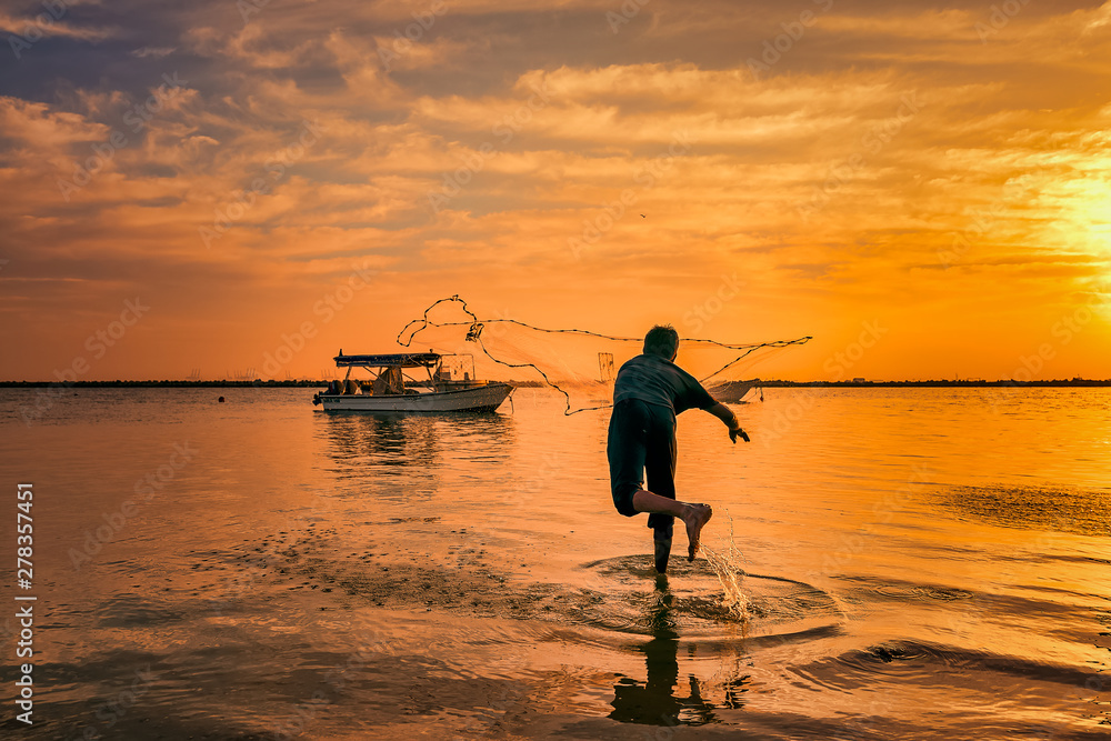 Silhouettes of the fishermen throwing fishing net during sunset in Dammam seaside Saudi Arabia