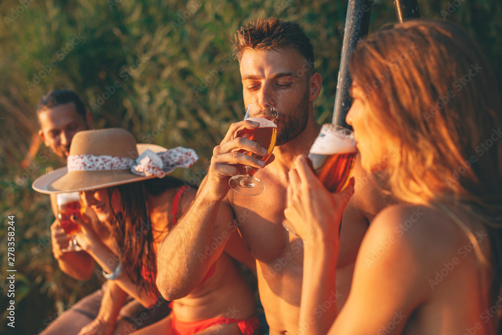Happy group of young people drinking beer on a dock by the river during the summer sunny day Happy group of young people drinking beer on a dock by the river during the summer sunny day