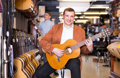 male customer deciding on acoustic guitar in musical shop