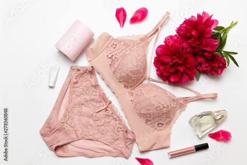 Female elegant pink lace bra, flat peony, lipstick, hand cream and barrette on a white background, flat lay.