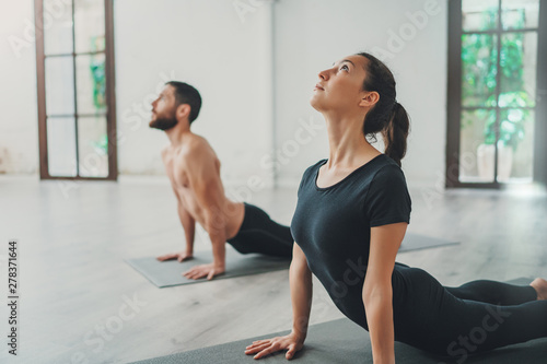 Young sportive man and woman are practicing yoga exercises in the studio. Couple of young sporty people practicing yoga lesson with partner.