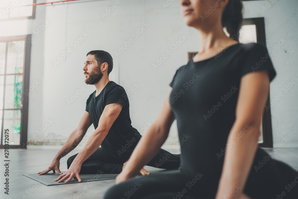 Yoga Practice Exercise Class Concept. Two beautiful people doing exercises.Young woman and man practicing yoga indoors Yoga Practice Exercise Class Concept. Two beautiful people doing exercises.Young woman and man practicing yoga indoors