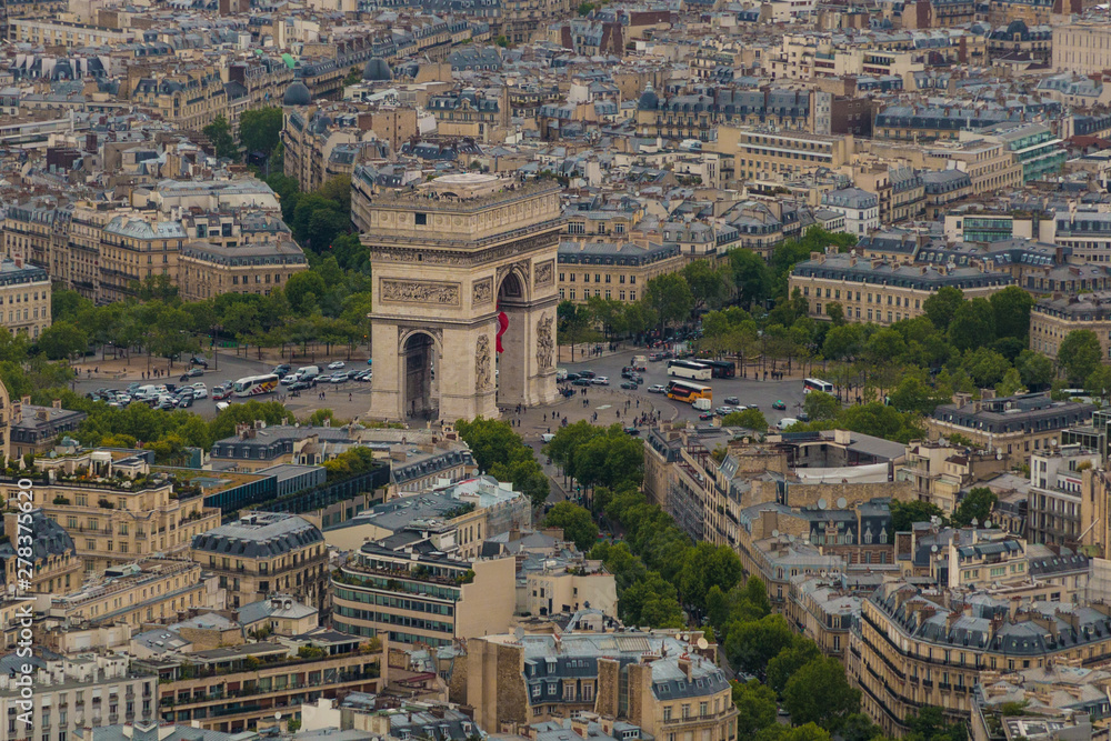 Great aerial view of the Arc de Triomphe de l'Étoile in Paris and the traffic on the roundabout of which the monument is the centre. Tourists walking at the base and on the roof of the arch.