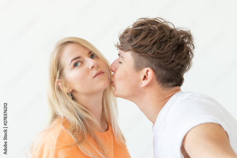 Charming young couple cute blond girl girl take a selfie posing over white background. Concept a young couple of teenagers or millennials In love.