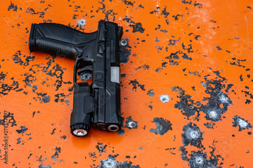 Modern black pistol on bright orange background with bullet marks