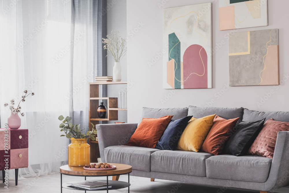 Yellow, orange, black and brown pillows on comfortable grey scandinavian  sofa in bright living room interior with abstract paintings on the wall  Stock Photo | Adobe Stock