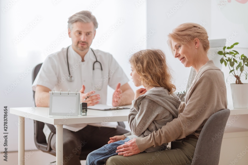 Mom and cute sick son in front of the handsome pediatrician's desk Mom and cute sick son in front of the handsome pediatrician's desk