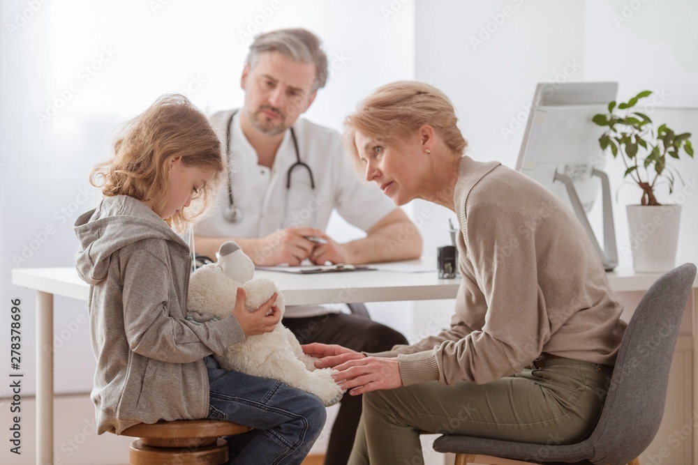 Sad girl with teddy bear and worried grandmother at pediatrician's office Sad girl with teddy bear and worried grandmother at pediatrician's office