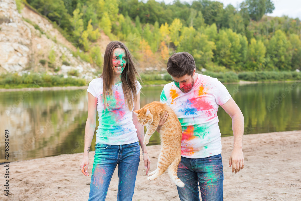 Festival holi, tourism and nature concept - Portrait of woman and man with cat covered multi-colored dust