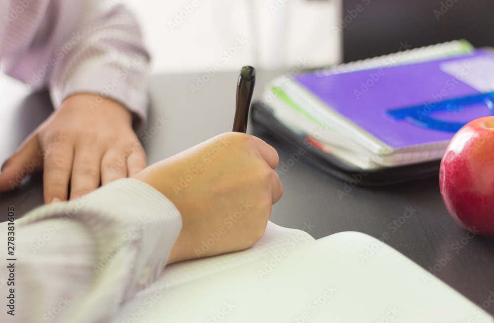 Fototapeta premium the student writes in a notebook, doing homework at his Desk