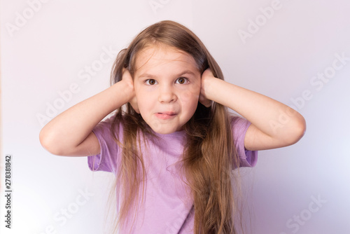 Little cute girl has closed his ears with his hands, with a funny expression on his face, on a light background
