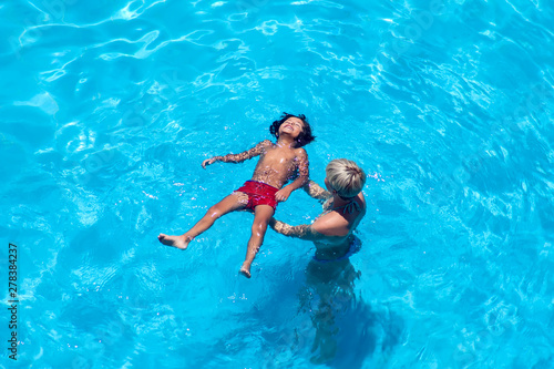 Mother teaches her sun swim in the pool.