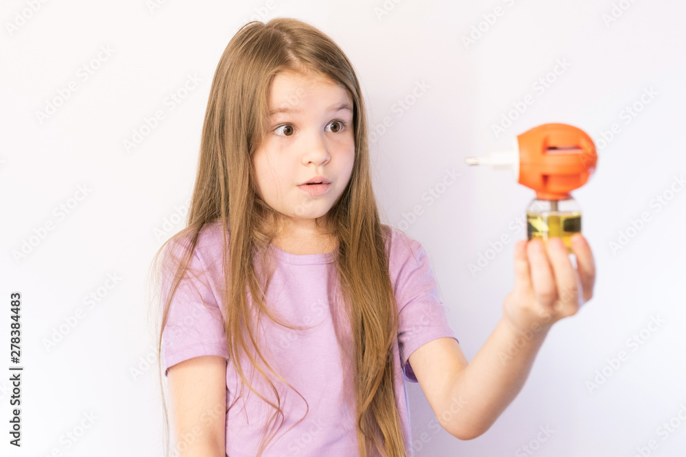 © Artsiom P - Little girl holding a fumigator from mosquitoes and stares at him, on a light background © Artsiom P - Little girl holding a fumigator from mosquitoes and stares at him, on a light background