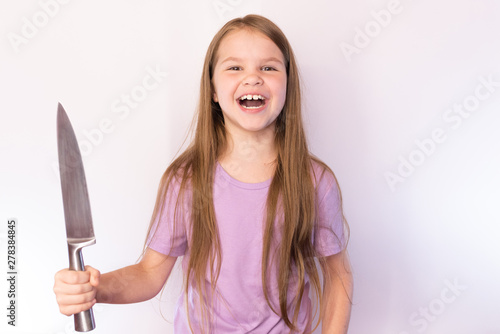 A little girl with a large kitchen knife  in a lavender shirt and with her hair  laughs evilly  on a light background