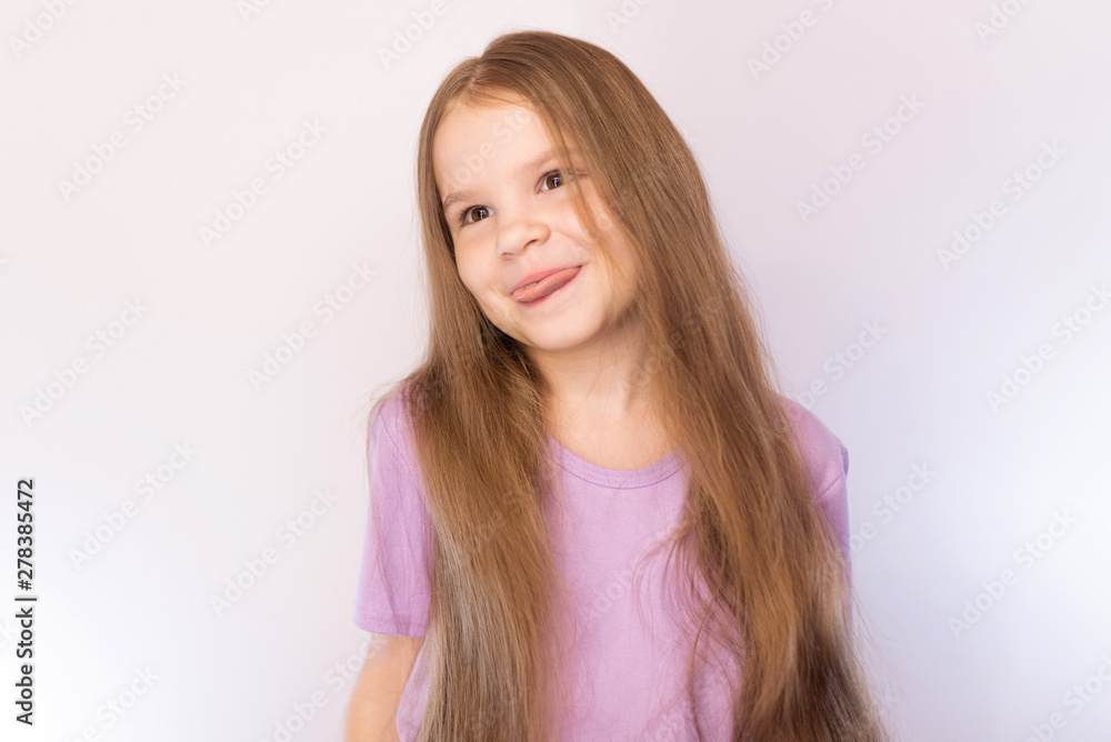 Cute little girl in a lavender shirt and with her hair, bowed his head to the side, shows the tongue on a light background Cute little girl in a lavender shirt and with her hair, bowed his head to the side, shows the tongue on a light background
