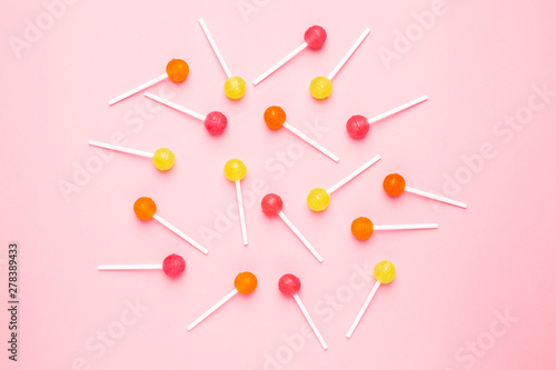 Pink, orange and yellow sweet candy lolipop on a pastel pink background