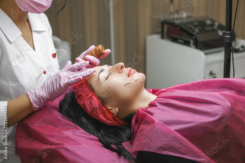 Cosmetologist making face care procedure. Specialist applying face mask to her client. Dermatology treatment. Facial peeling.