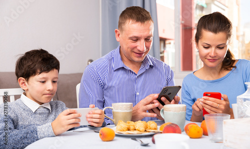 Parents and teen son using phones at kitchen