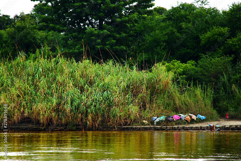 Women drying her colorful laundry on high grass on the shore of a river in Myanmar/Birma.