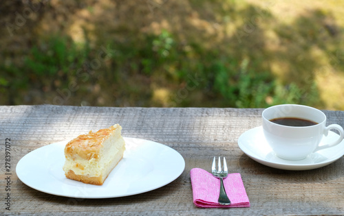 Close up front view of a piece of classic tradiional German bee sting cake (Biienenstich) with caramelized almond. A cup of black coffee is in the top right corner.