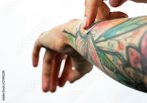 Female tattooed hands hold a jar of cream. Fingers apply cream to skin. Close up