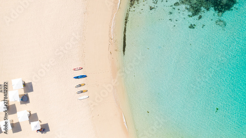 Beach umbrellas and deck chairs on the white beach. White sandy beach and clear turquoise lagoon, top view.