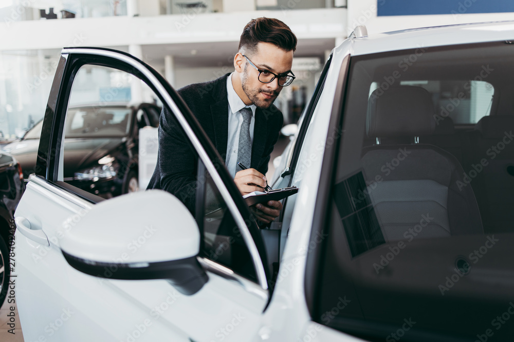 Car seller working in showroom and quality control checking of car details for the last time before buyer comes. Car seller working in showroom and quality control checking of car details for the last time before buyer comes.