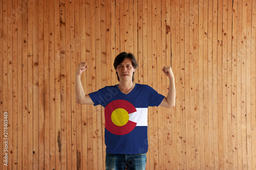 Man wearing Colorado flag color of shirt and standing with raised both fist on the wooden wall background.