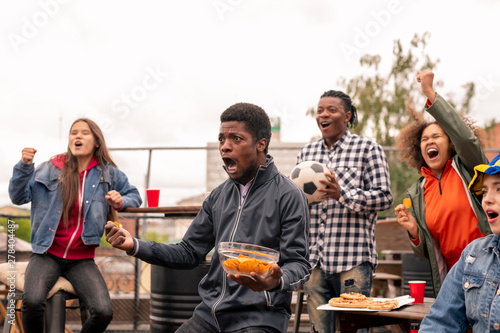 Multi-ethnic group of ecstatic youth with snack shouting during broadcast