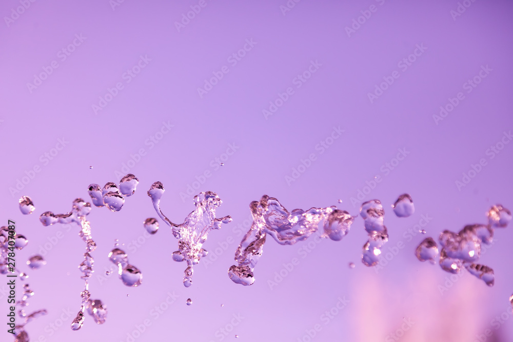 Water droplets frozen in the air with splashes and chain bubbles on a pink and purple isolated background in nature. Clear and transparent liquid symbolizing health and nature.