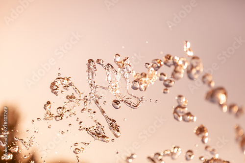 Water droplets frozen in the air with splashes and chain bubbles on a golden and bronze isolated background in nature. Clear and transparent liquid symbolizing health and nature. photo
