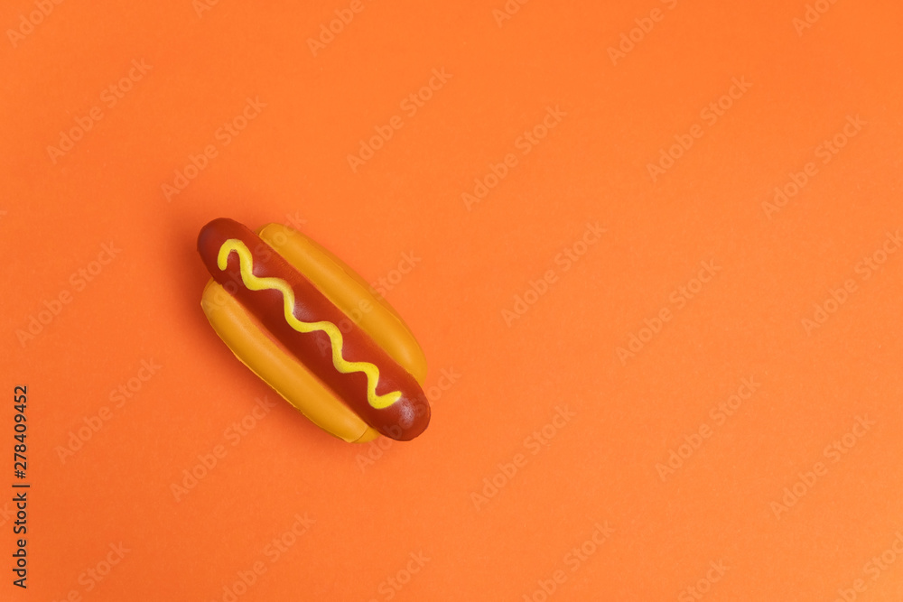 Artificial plastic hot dog on orange background with copy space. Harmful plastic food concept. Unhealthy eating