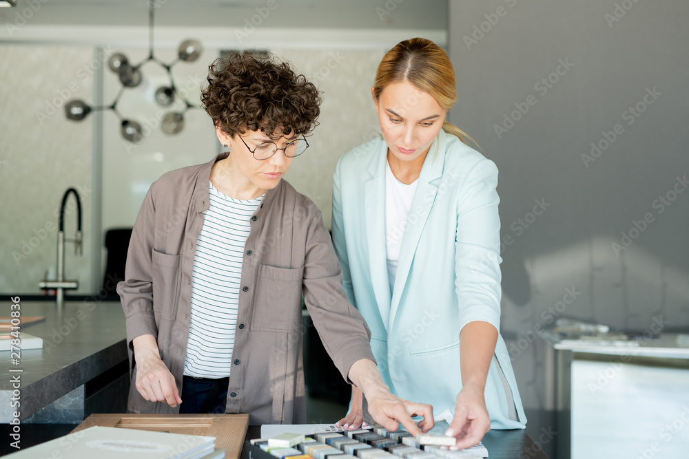 Pretty young client of interior design studio looking at one of samples Pretty young client of interior design studio looking at one of samples