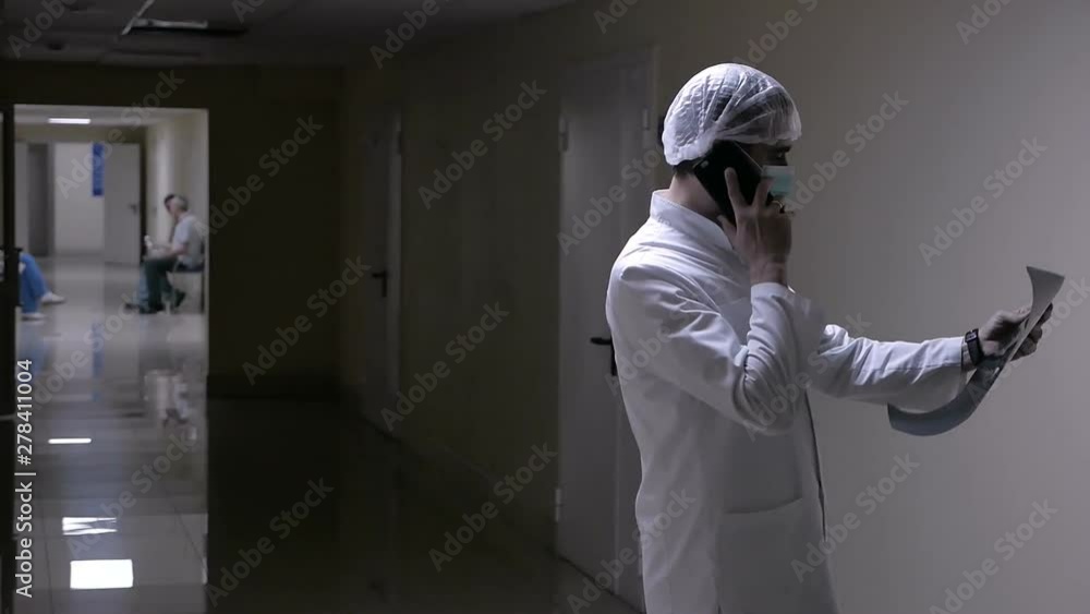doctor talking on the phone with a patient holding an x-ray in his hands walking down the corridor of the clinic discussing the problem by telephone doctor talking on the phone with a patient holding an x-ray in his hands walking down the corridor of the clinic discussing the problem by telephone