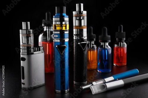 Electronic cigarettes and bottles with vape liquid on black background