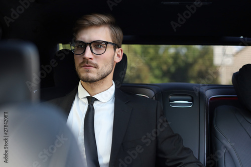 Thoughtful confident businessman in full suit with eyewear looking away while sitting in the car. © ty