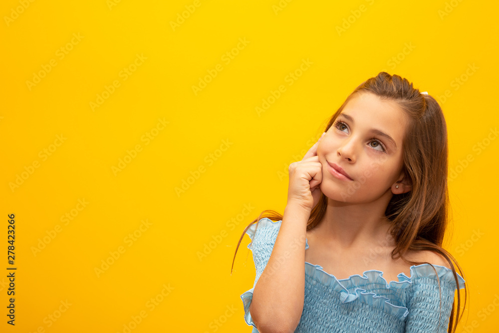 Beautiful female half-length portrait isolated on yellow studio background. Little emotional Brazilian girl. Facial expression, human emotions, advertising concept. Thinking, looking up. Beautiful female half-length portrait isolated on yellow studio background. Little emotional Brazilian girl. Facial expression, human emotions, advertising concept. Thinking, looking up.