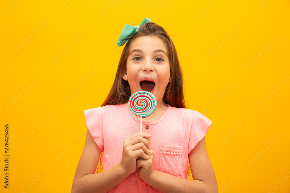 © Nexa - The child is holding a lollipop. Childish joy is sweetness. Little girl on yellow background.