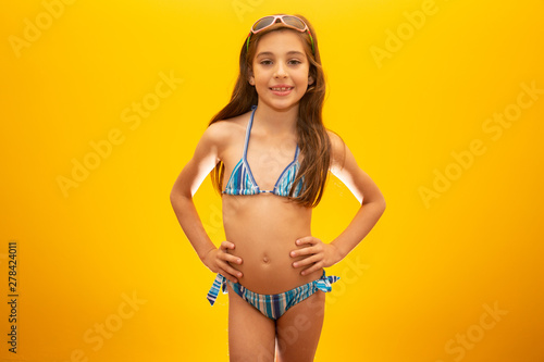 Child wearing bikini on yellow background. Concept of summer, beach and pool. photo