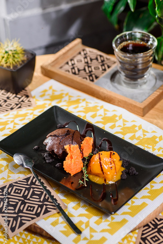 Beautiful dessert serving - chocolate cake and mango ice cream with berry syrup on a black plate on the table in the restaurant. Close up. Space.